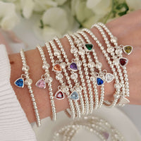 A close up photograph of a woman's wrist wearing multiple Bella Jane beaded sterling silver beaded stacking bracelets, all featuring a different coloured birthstone charms