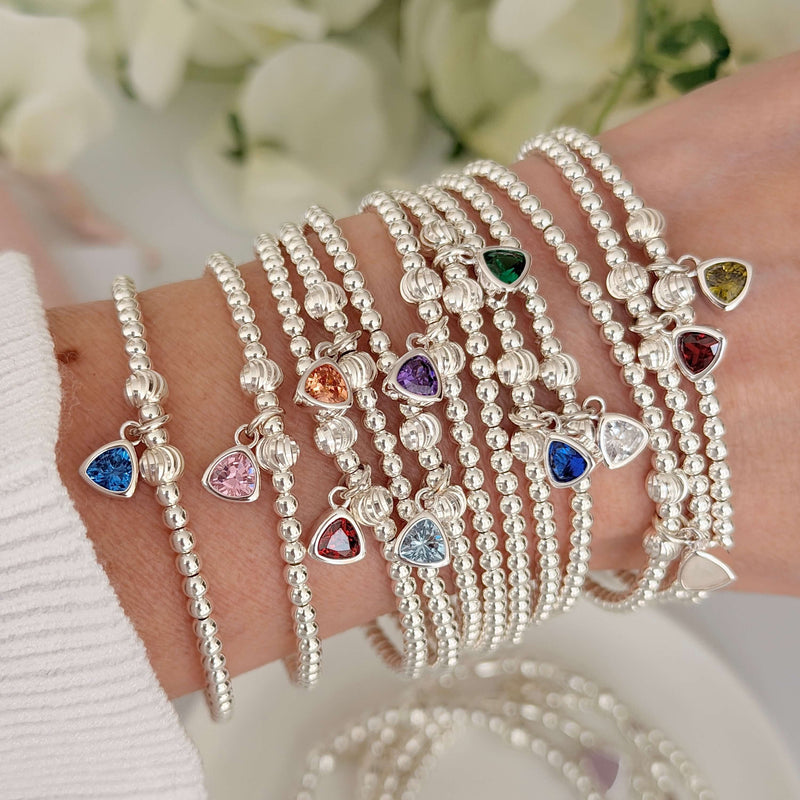 A close up photograph of a woman's wrist wearing multiple Bella Jane beaded sterling silver beaded stacking bracelets, all featuring a different coloured birthstone charms