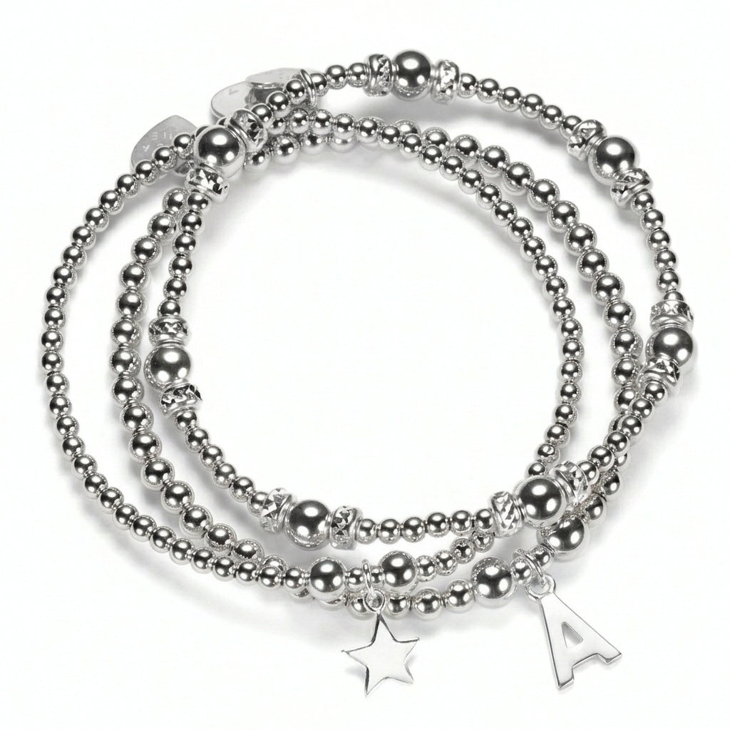 The Icons Stack of three sterling silver beaded bracelets with a star charm and a sterling silver initial 'A' charm, on a white background