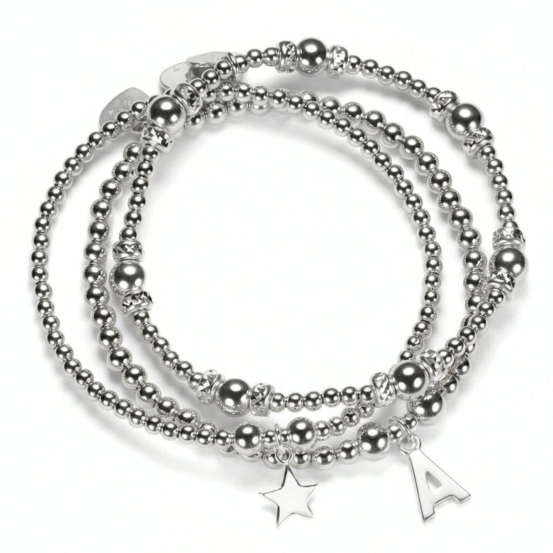 The Icons Stack of three sterling silver beaded bracelets with a star charm and a sterling silver initial 'A' charm, on a white background