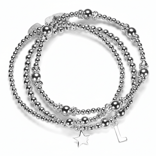 Stack of silver beaded bracelets with star and initial charms on a white background