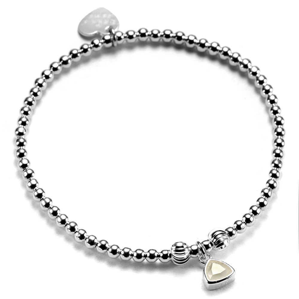 A close up of a handmade sterling silver beaded stacking bracelet, featuring an moonstone coloured birthstone charm to represent June