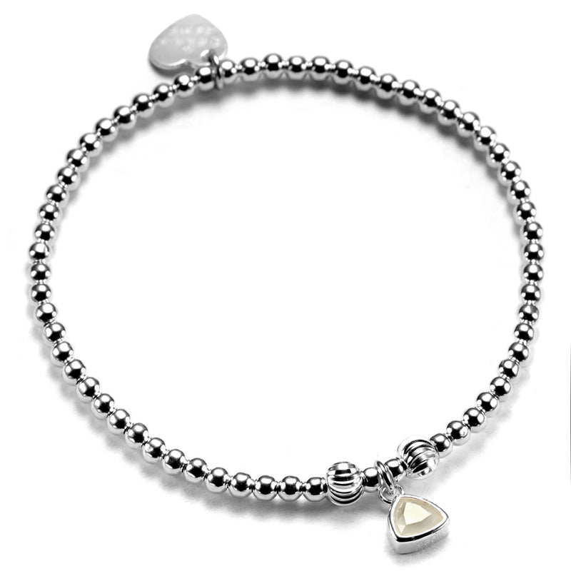 A close up of a handmade sterling silver beaded stacking bracelet, featuring an moonstone coloured birthstone charm to represent June