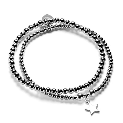 A silver stacking bracelet duo with one plain stacking bracelet and one featuring a silver star charm, on a white background