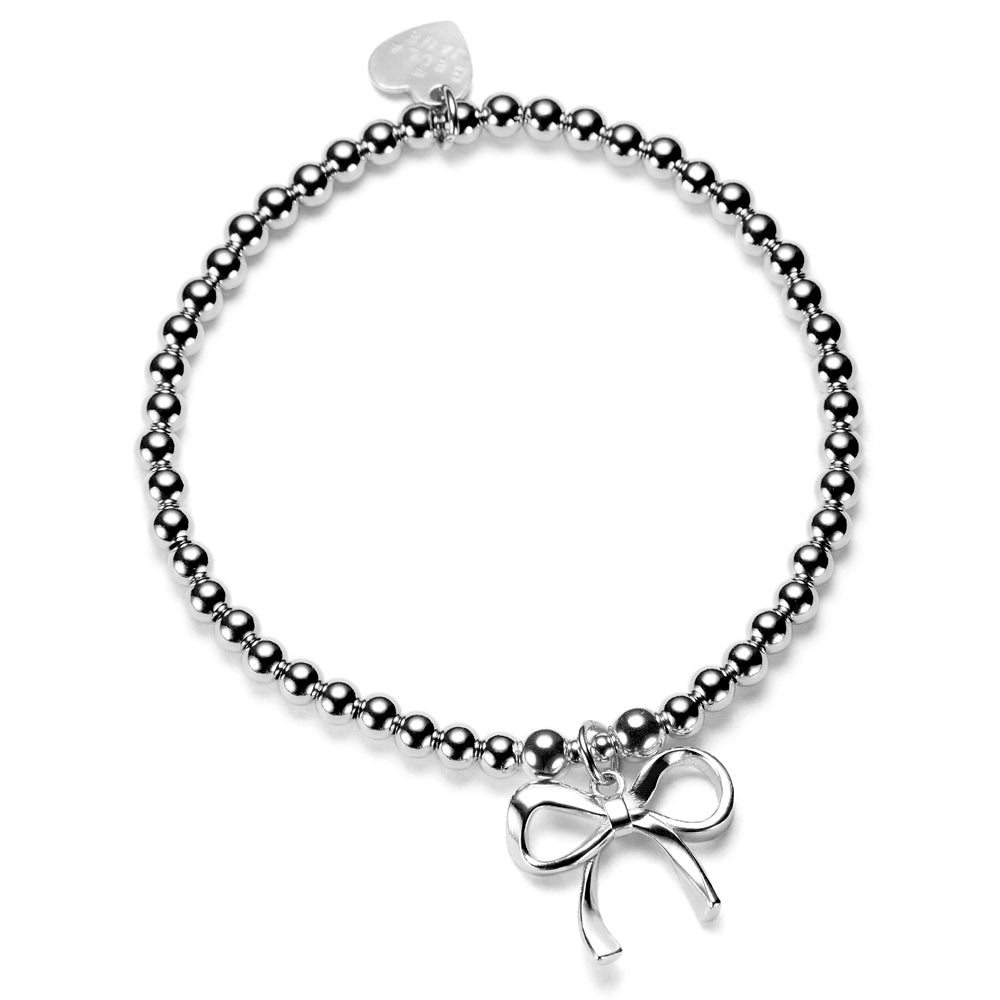 A close up shot of a sterling silver beaded bracelet, featuring a large bow charm.