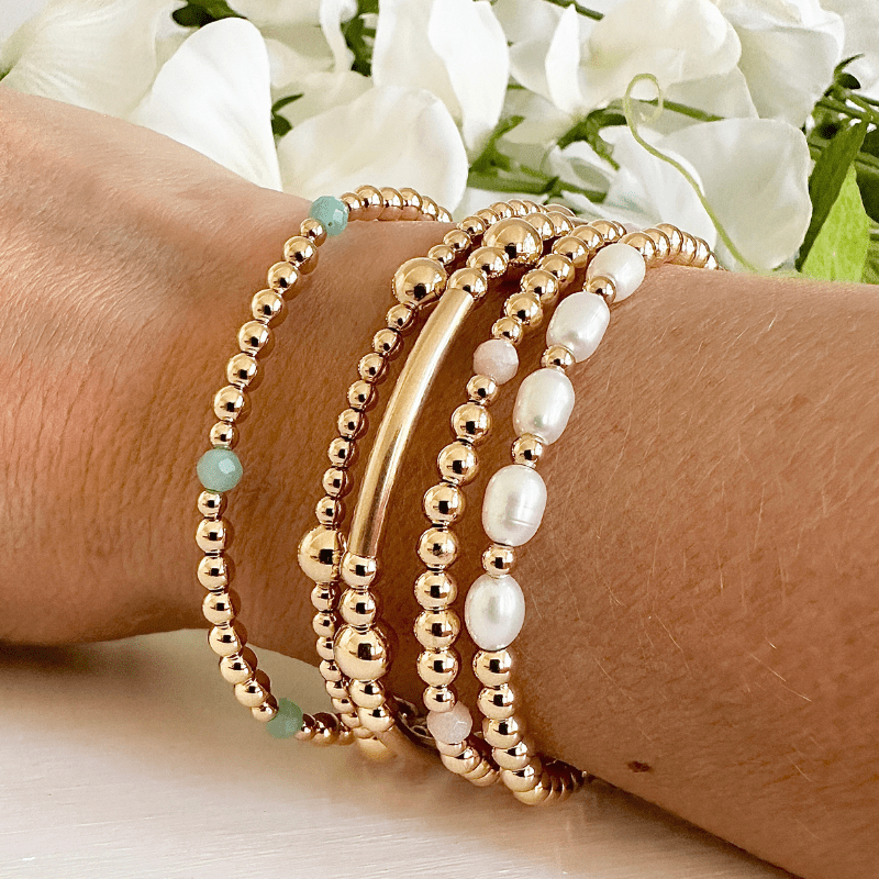 Gold beaded bracelets on a wrist with a floral background