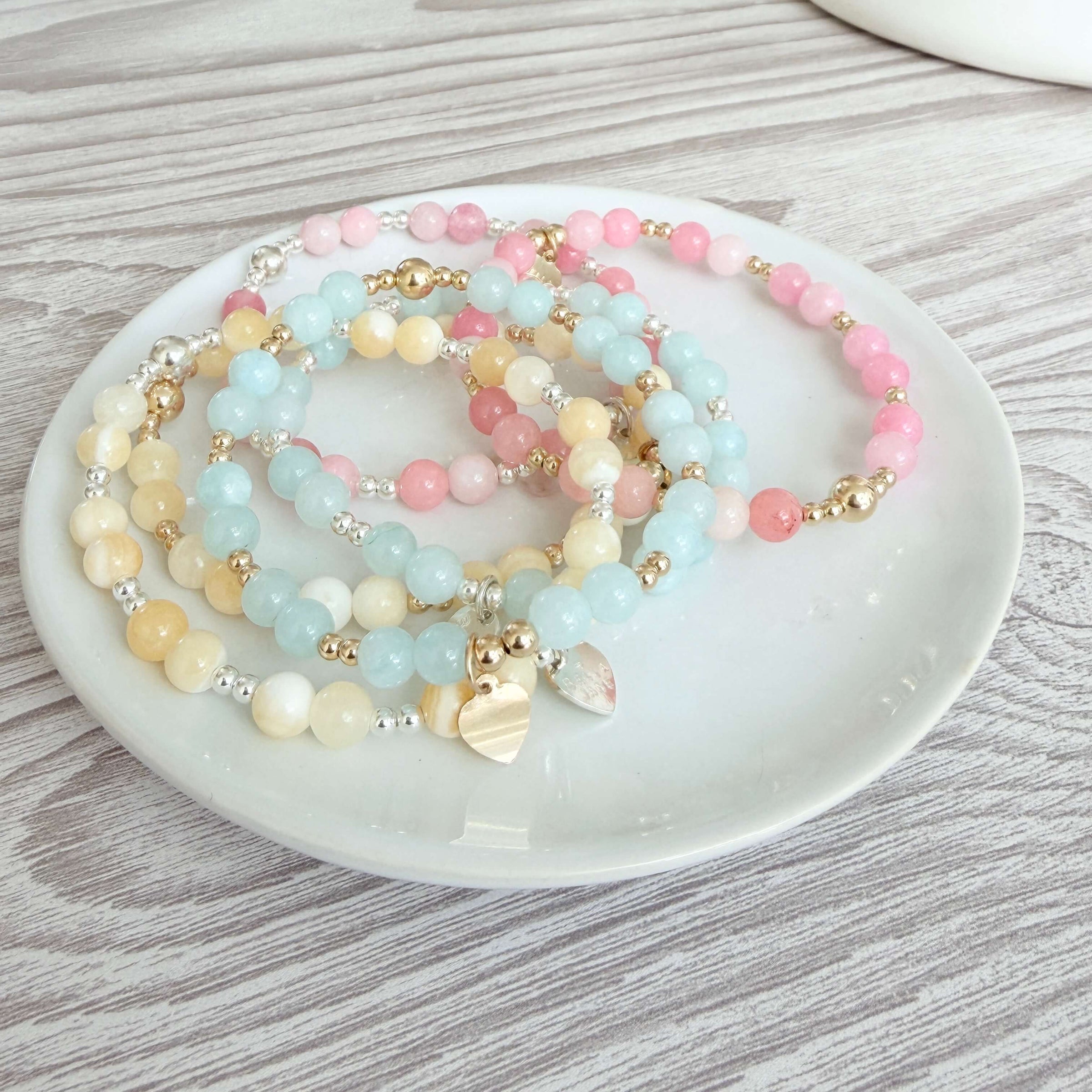 Set of Bella Jane Summer 2026 pastel coloured beaded stacking bracelets on a white dish with a wooden background