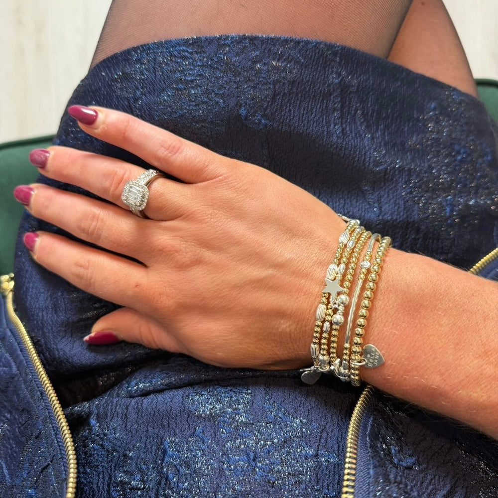 Hand with stacking bracelets, against a blue textured fabric background.