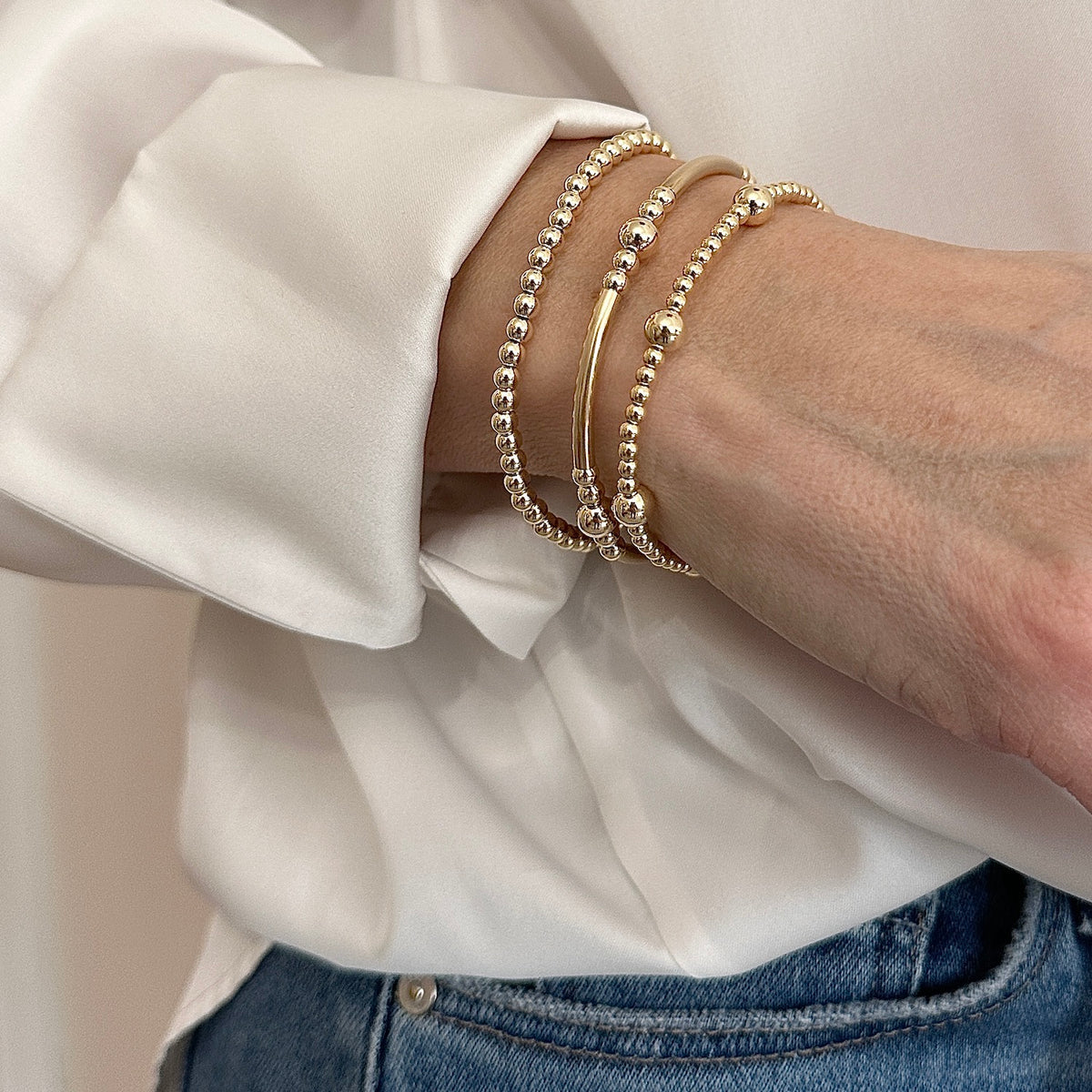 A model wearing a stack of three gold-filled, beaded stacking bracelets