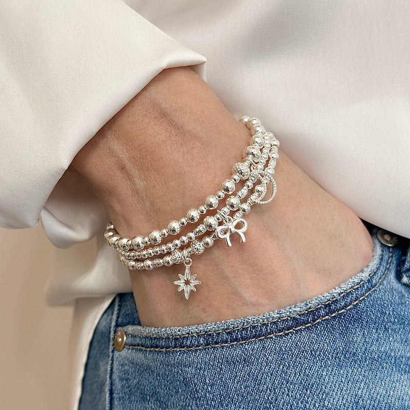 A close up of a lady's wrist wearing 3 beaded stacking bracelets with charms, with hand in jeans pocket.