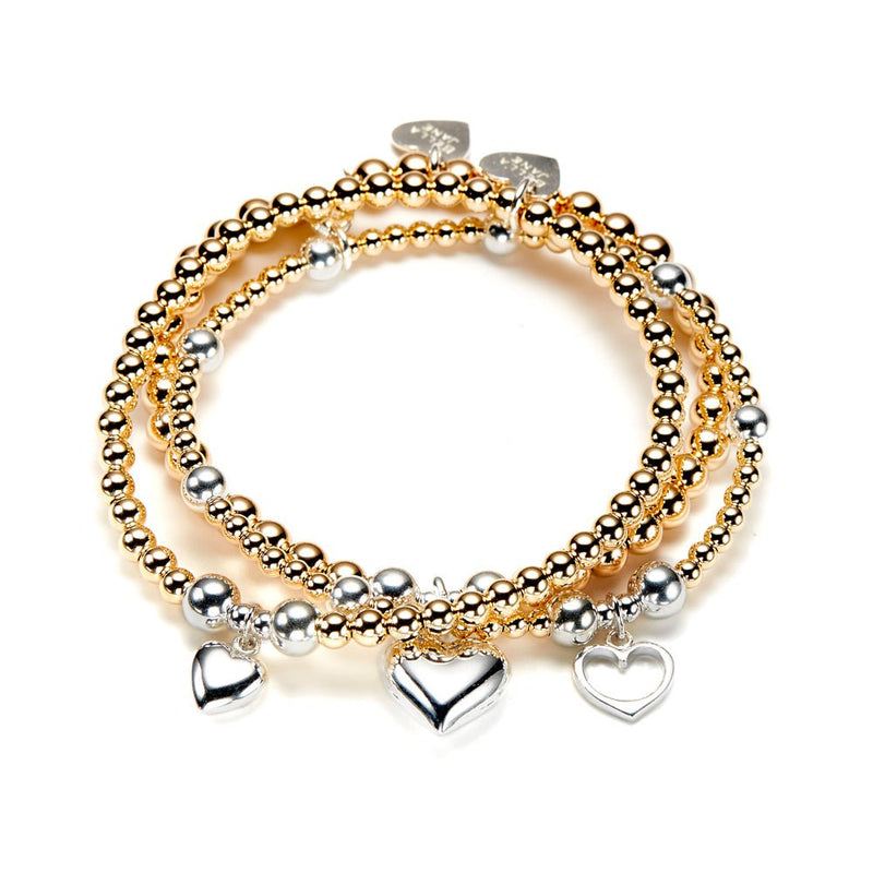 A stack of 3 gold beaded bracelets with silver heart charms on a white background