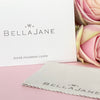 A silver polishing cloth with the Bella Jane brand logo displayed beside some pink roses.