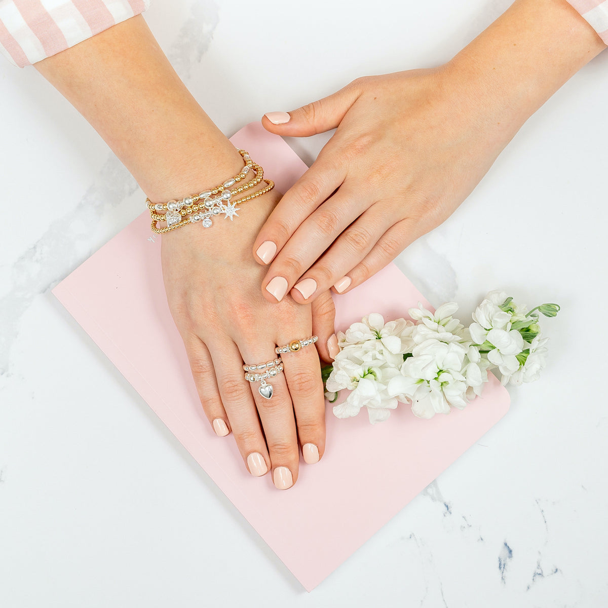 a close up of a hand wearing a stack of three gold and silver mixed metal stacking bracelets with 3 stacking rings on the fingers.