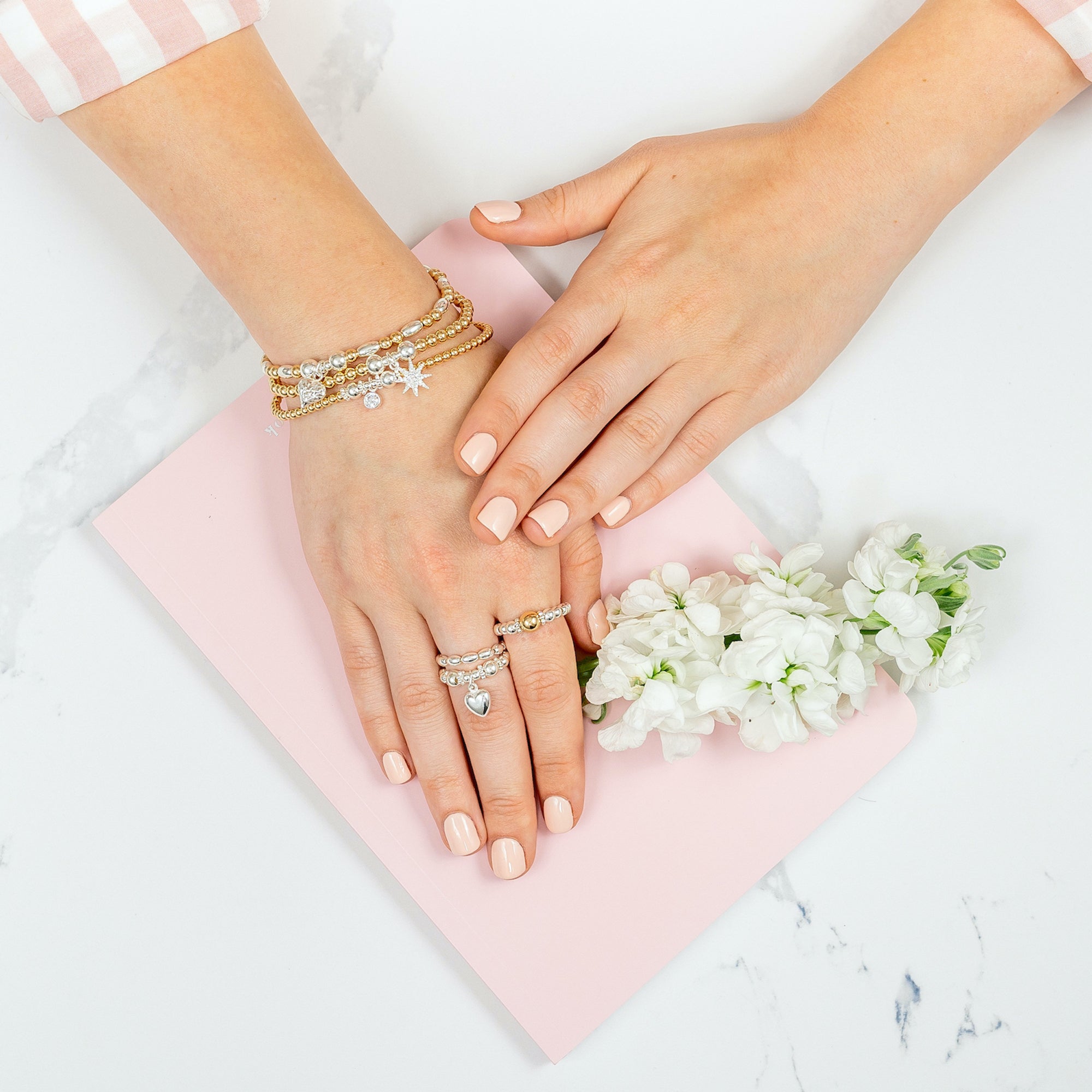 a close up of a hand wearing a stack of three gold and silver mixed metal stacking bracelets with 3 stacking rings on the fingers.