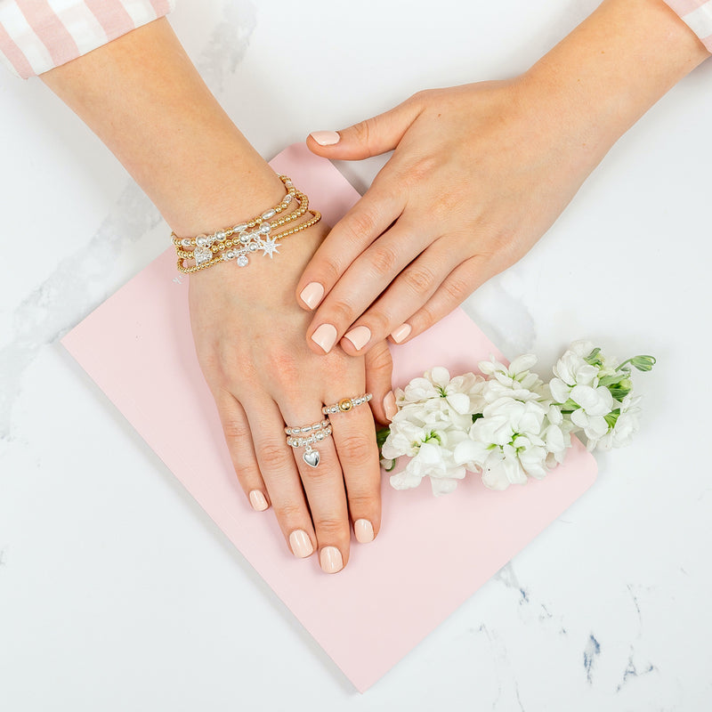 a close up of a hand wearing a stack of three gold and silver mixed metal stacking bracelets with 3 stacking rings on the fingers.