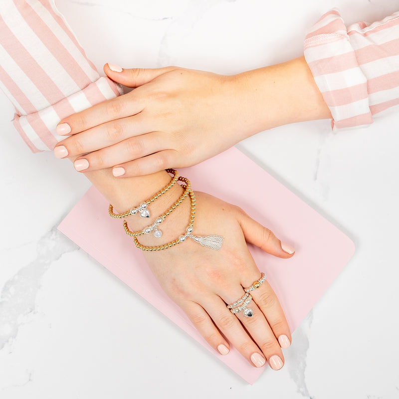 Close up of a lady's hand on a pink notebook, wearing gold and silver stacking bracelets with beaded stacking rings on fingers