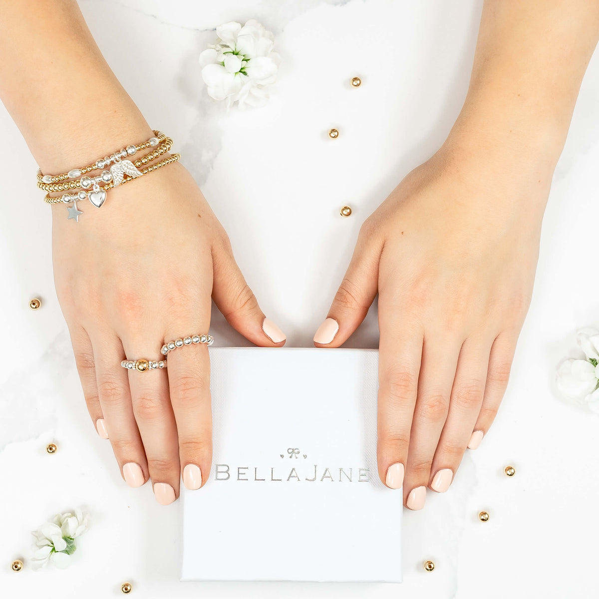 Hands wearing silver and gold mixed-metal beaded stacking bracelets and rings on a white background with a 'Bella Jane' branded box.