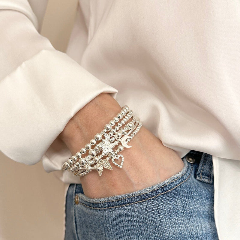 Silver charm stacking bracelets on a wrist with hand in jeans pocket