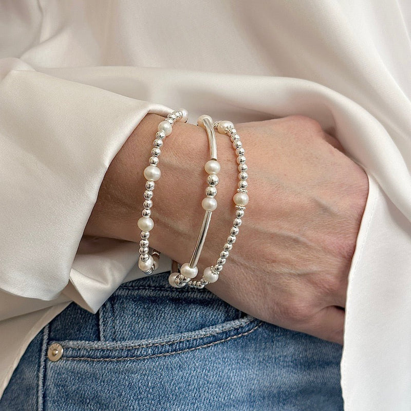 Hand wearing three sterling silver and pearl bracelets on a neutral background