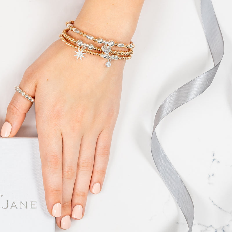 Close up of a lady's hand around a Bella Jane white box, wearing 3 beaded gold and silver mixed metal stacking bracelets with charms