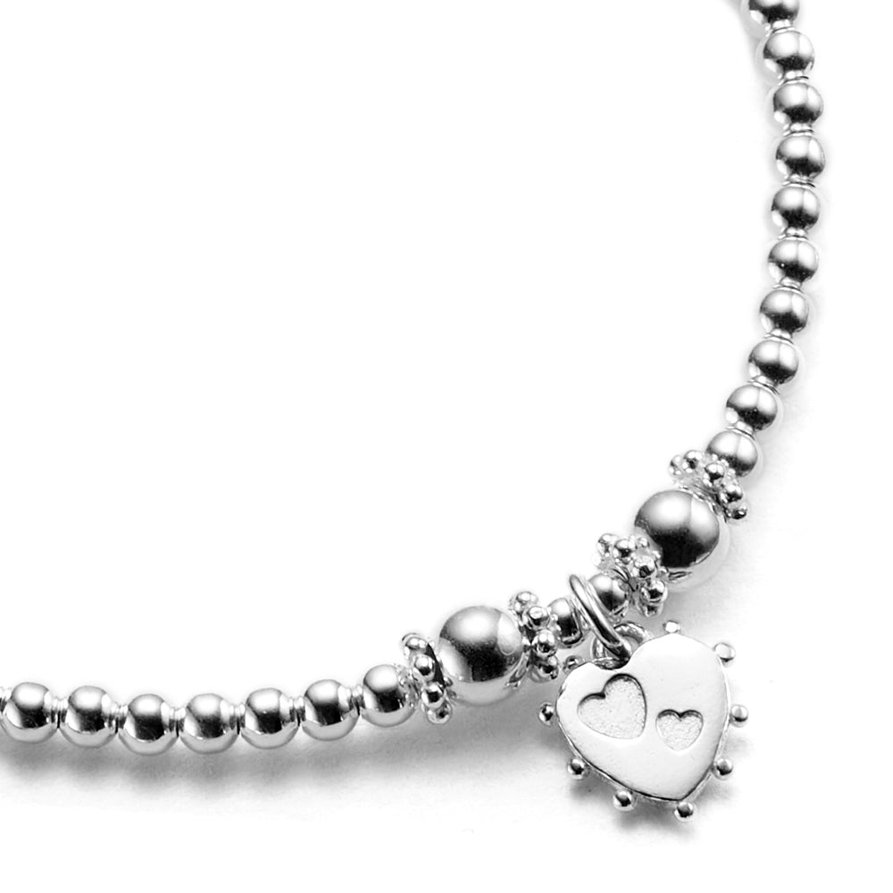 The reverse side of the pink enamel heart charm on a beaded bracelet, featuring two tiny stamped out hearts.