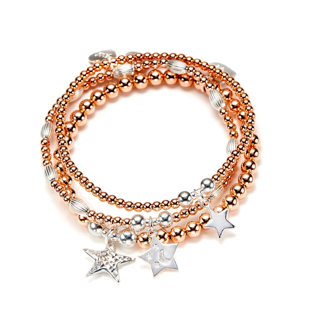 Stack of rose gold and silver beaded bracelets with star charms on a white background